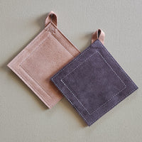Two square potholders, one tan and one dark brown, on a light gray background.