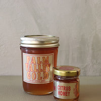 Two jars of honey labeled 'Palm Valley Gold' and 'Citrus Honey' on a neutral background.