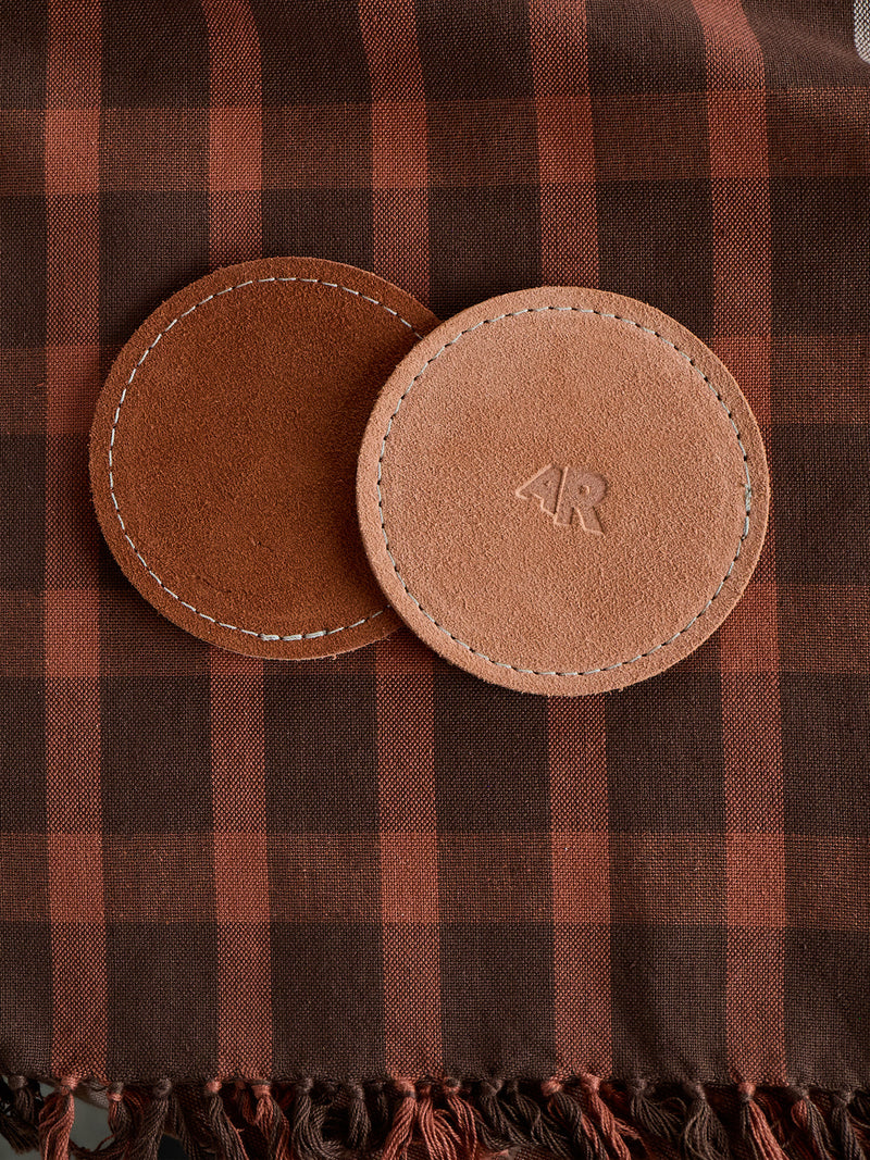 Two brown leather coasters with a logo on a plaid fabric background