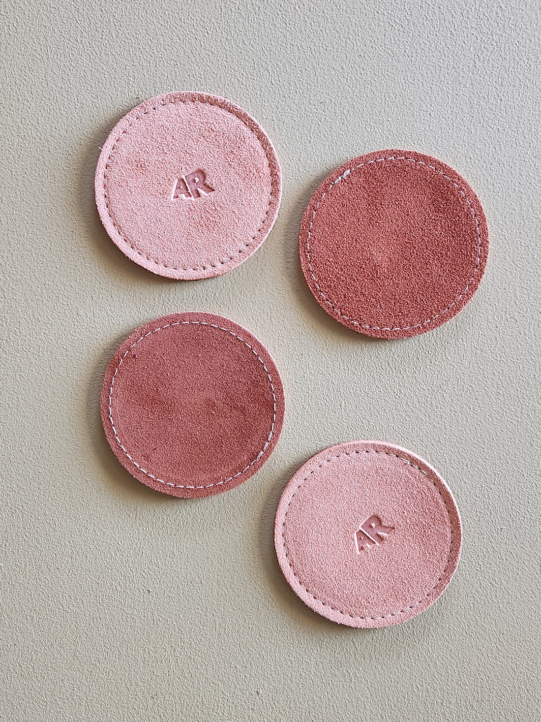 Four pink circular coasters with initials on a light gray background