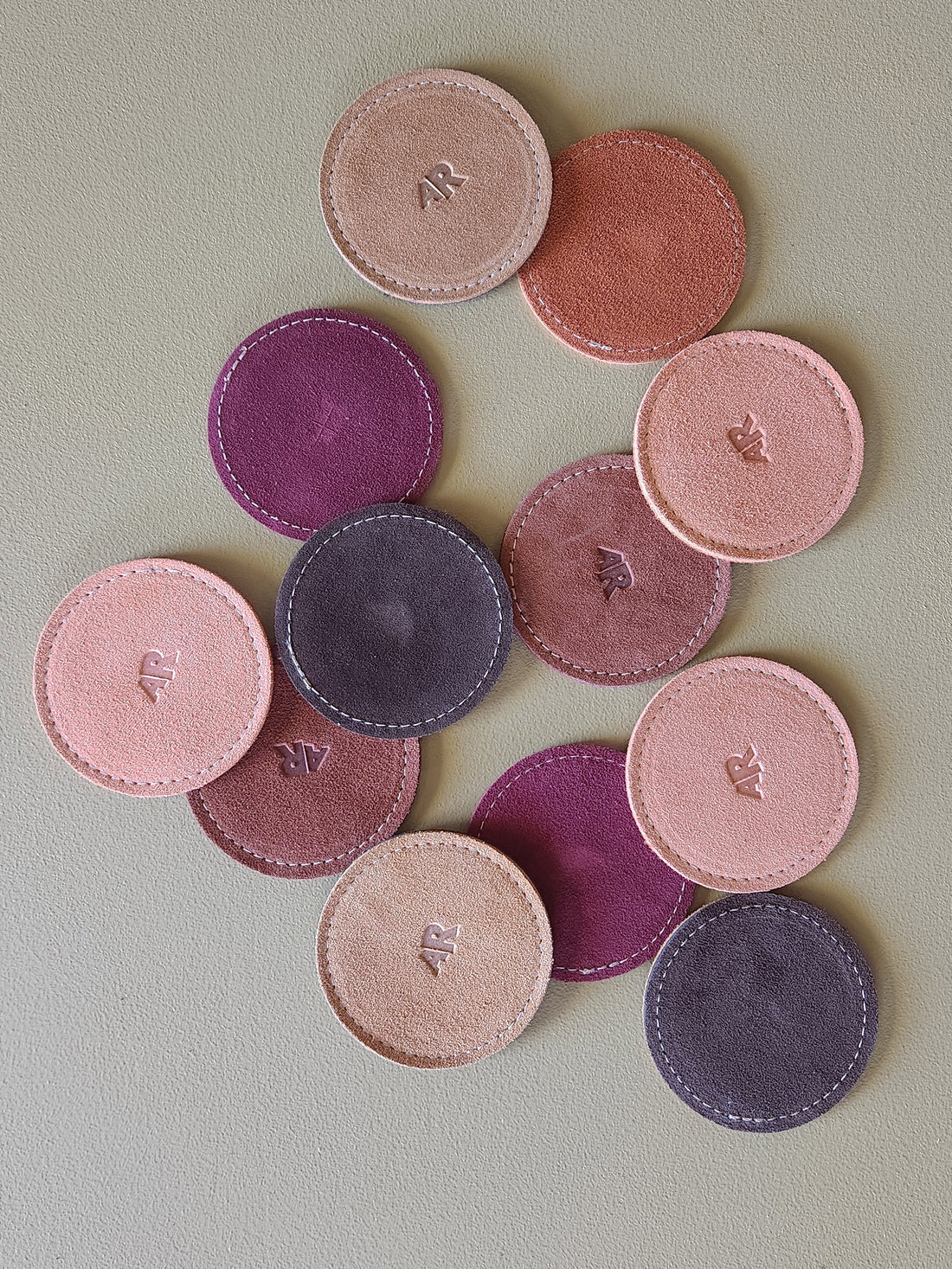 Set of round, suede coasters in various pink and purple shades on a light green background.