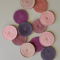 Set of round, suede coasters in various pink and purple shades on a light green background.