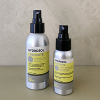 Two silver Hydrosol Creosote bottles with black spray tops and yellow labels, standing on a beige surface against a textured beige wall.