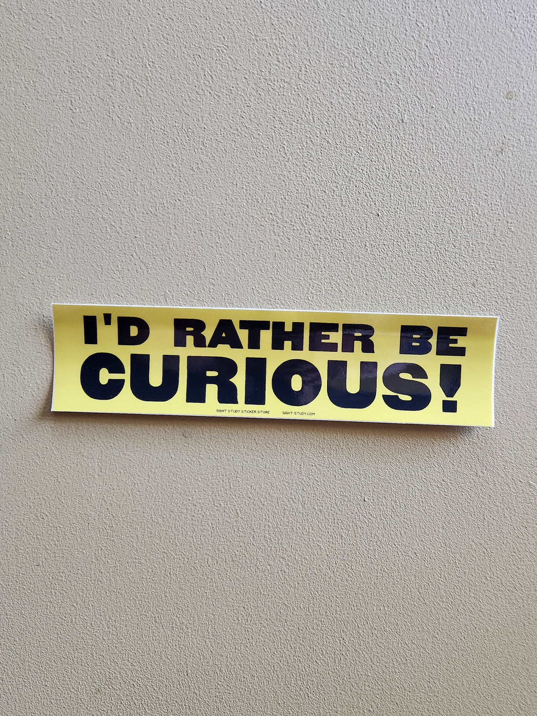 A yellow bumper sticker with bold black text reading &