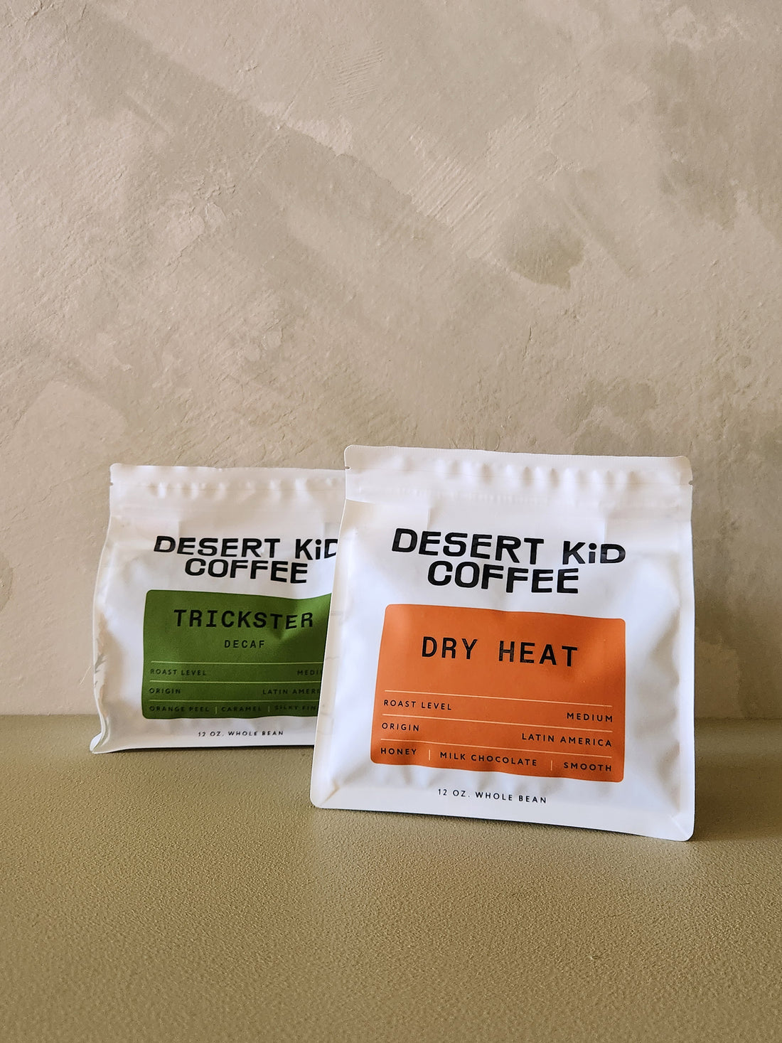 Two packages of Desert Kid Coffee on a beige surface with a beige background