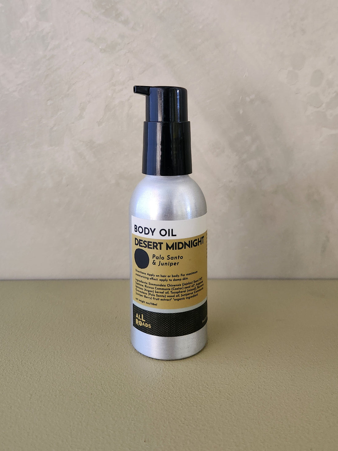 A bottle of body oil with a black pump and a silver bottle body, featuring a beige and black label that reads &