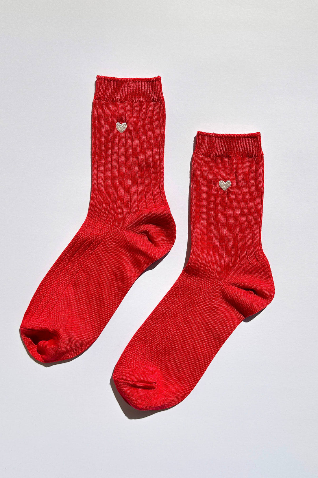 Pair of red socks with heart details on a light gray background