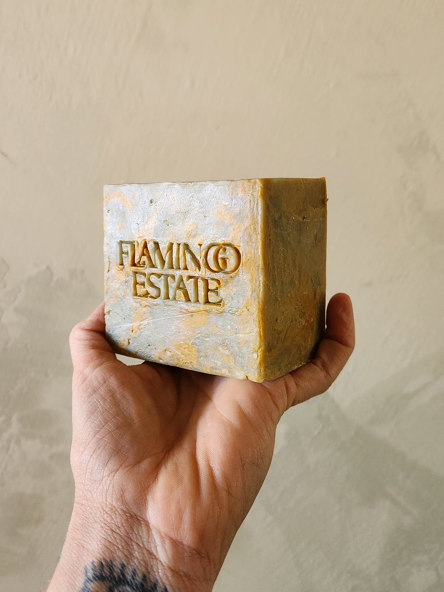 Hand holding a bar of soap with 'Flaming Estate' branding against a beige background