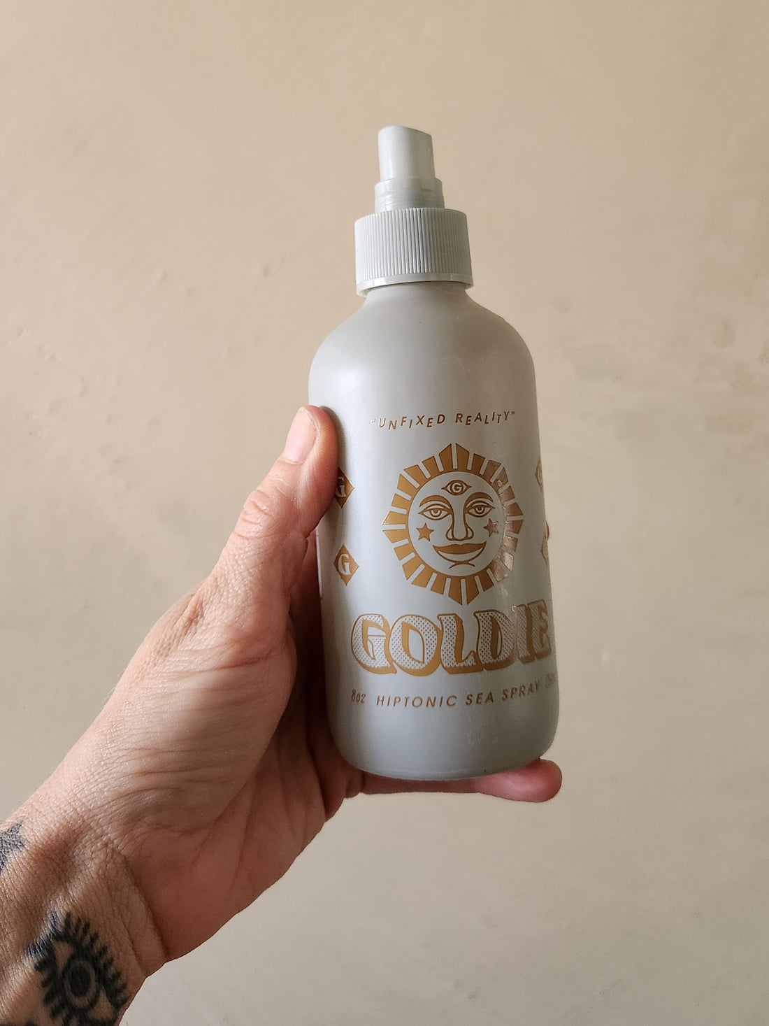 A hand holding a frosted white spray bottle labeled &
