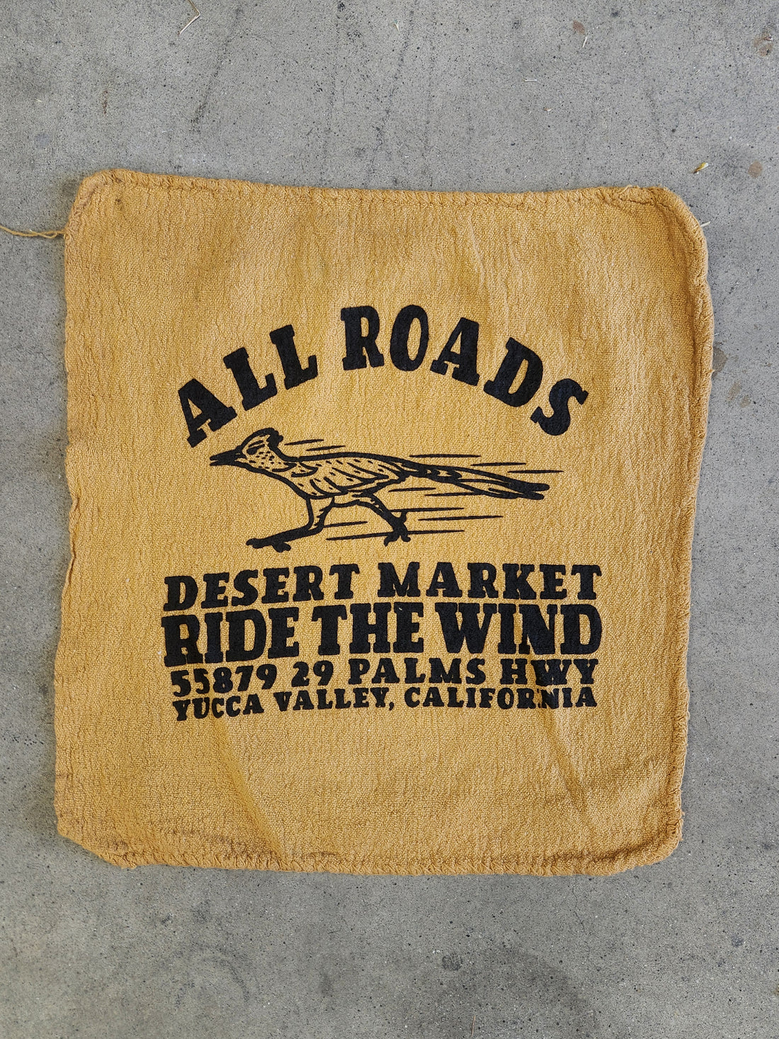Beige burlap bag with black text and a logo on a gray concrete surface