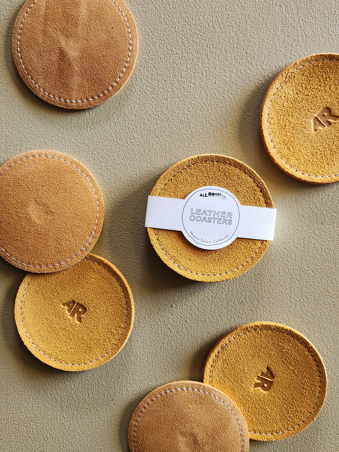 A set of round tan leather coasters with white stitching and embossed &