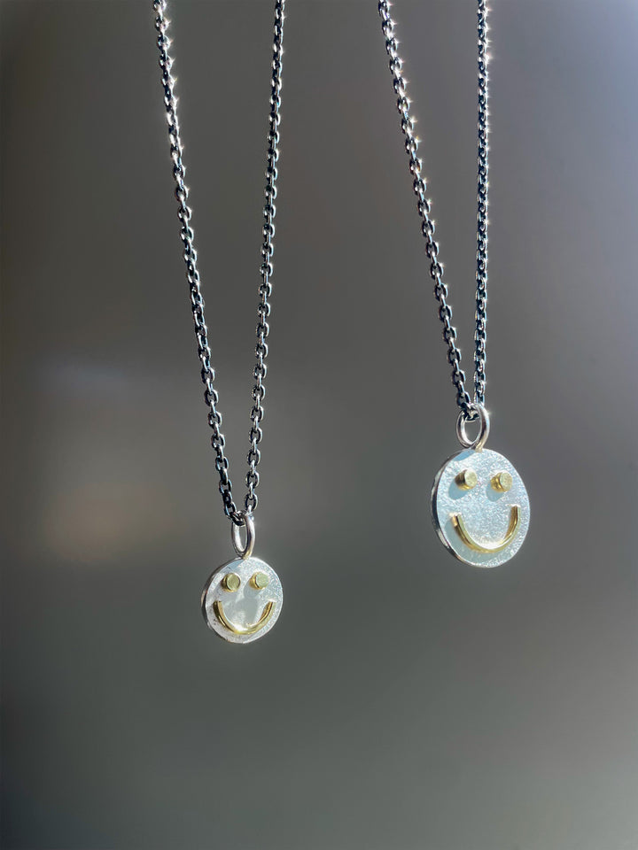 Two silver necklaces with smiley face pendants on a blurred gray background