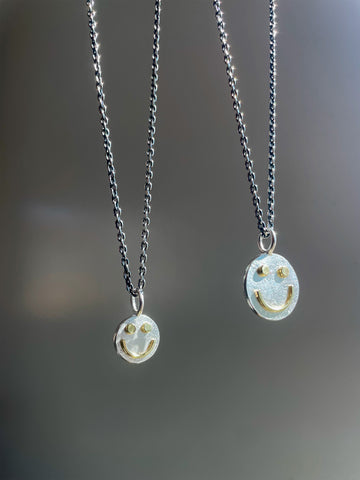 Two silver necklaces with smiley face pendants on a blurred gray background