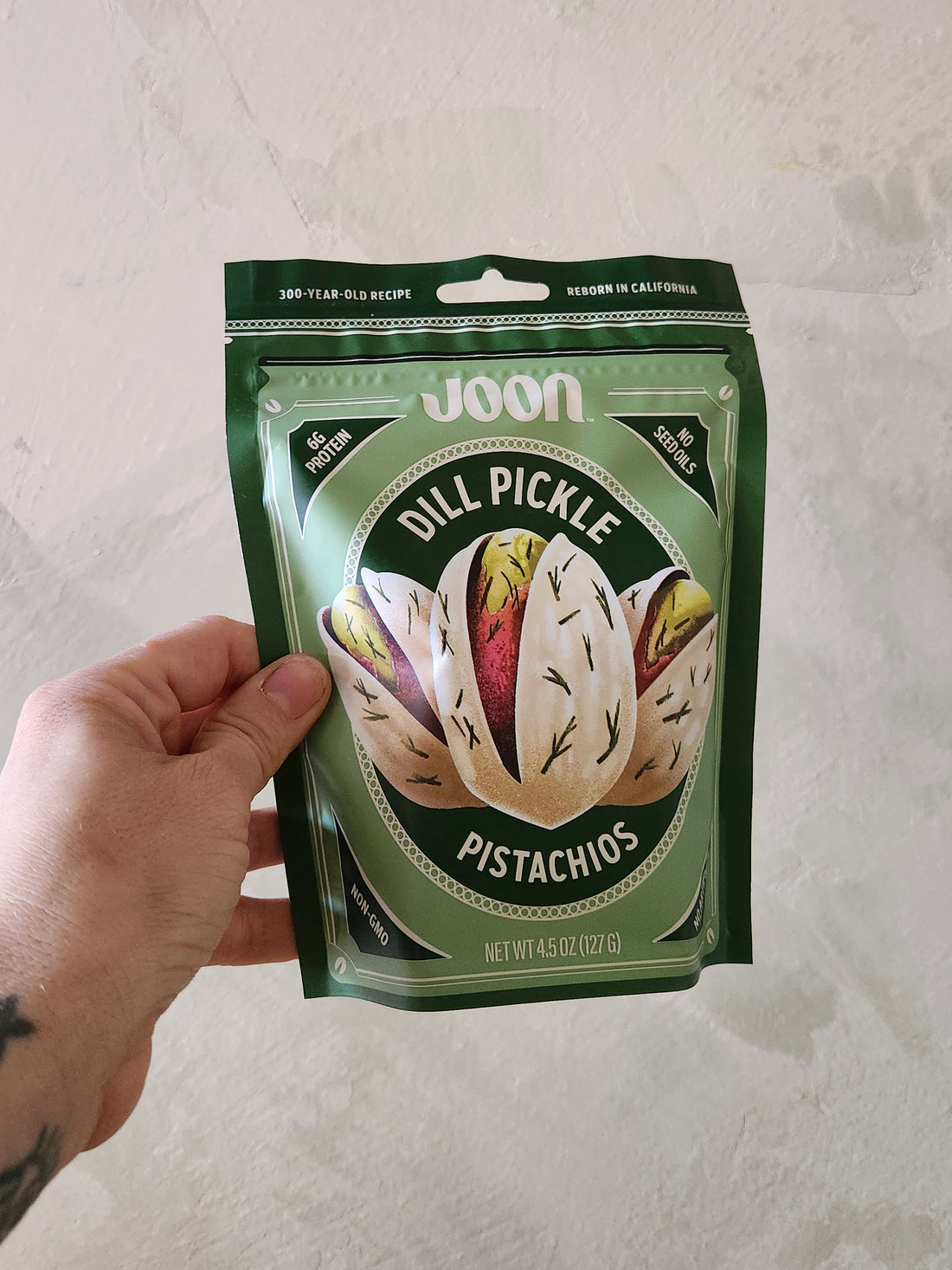 Hand holding a package of Joon Dill Pickle Pistachios on a light background