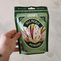 Hand holding a package of Joon Dill Pickle Pistachios on a light background
