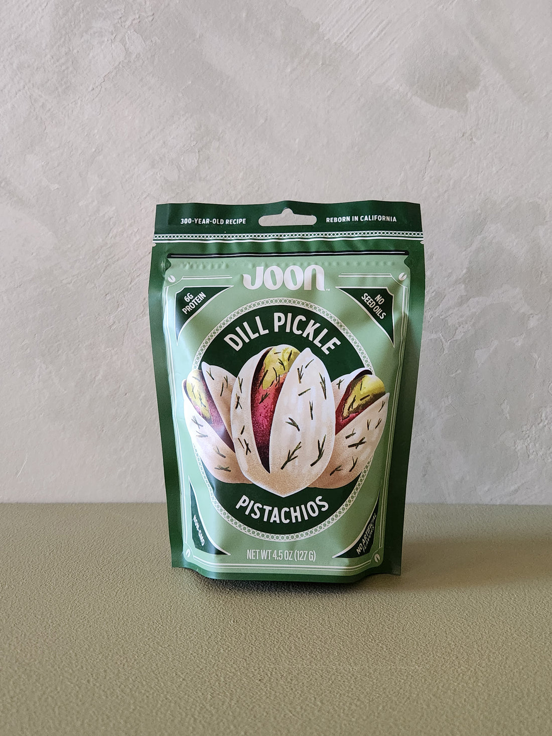 Packaged pistachios with dill pickle flavor on a neutral background