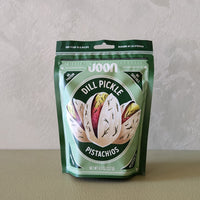 Packaged pistachios with dill pickle flavor on a neutral background
