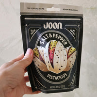 Hand holding a package of Joon Salt & Pepper Pistachios against a neutral background