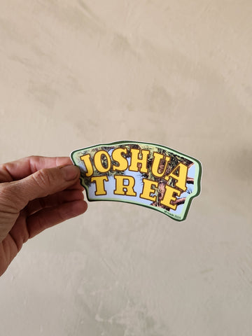 Hand holding a 'Joshua Tree' sticker against a beige background