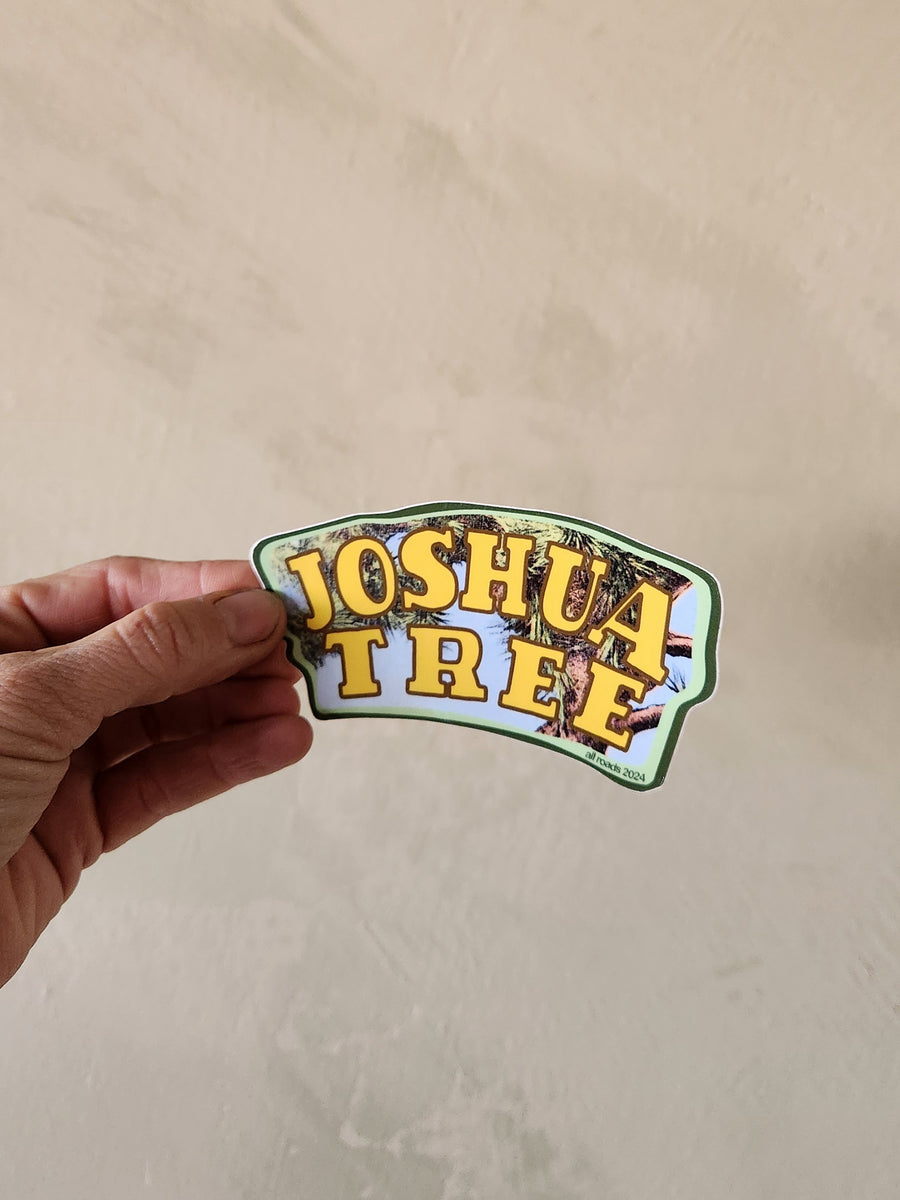 Hand holding a 'Joshua Tree' sticker against a beige background