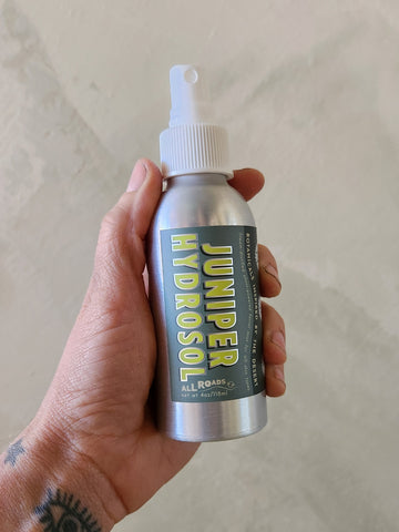 Hand holding a Juniper Hydrosol bottle against a neutral background