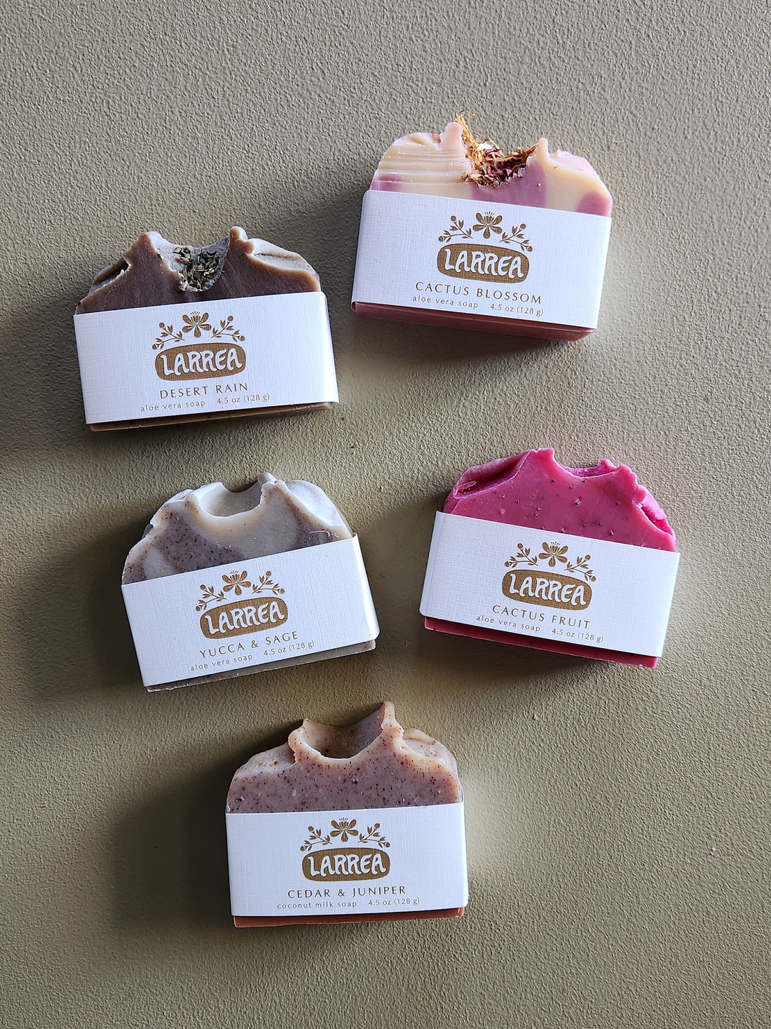 Five Larrea soap bars with labels on a beige background