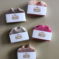 Five Larrea soap bars with labels on a beige background