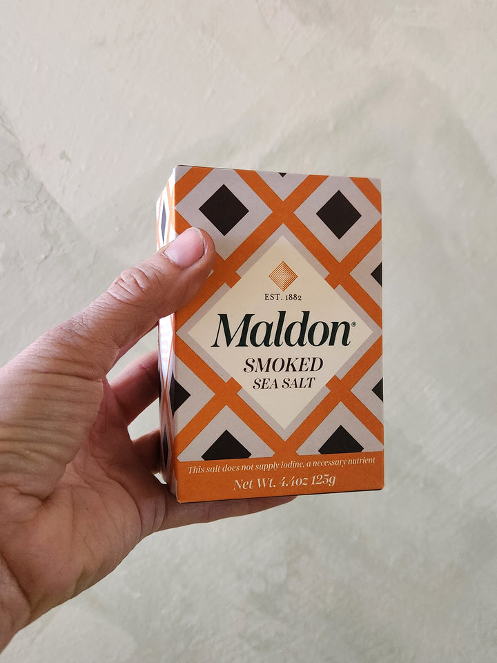 Hand holding a box of Maldon smoked sea salt against a light background