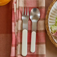 Silver fork and spoon on a pink and beige checkered napkin with a blurred plate of salad in the background.