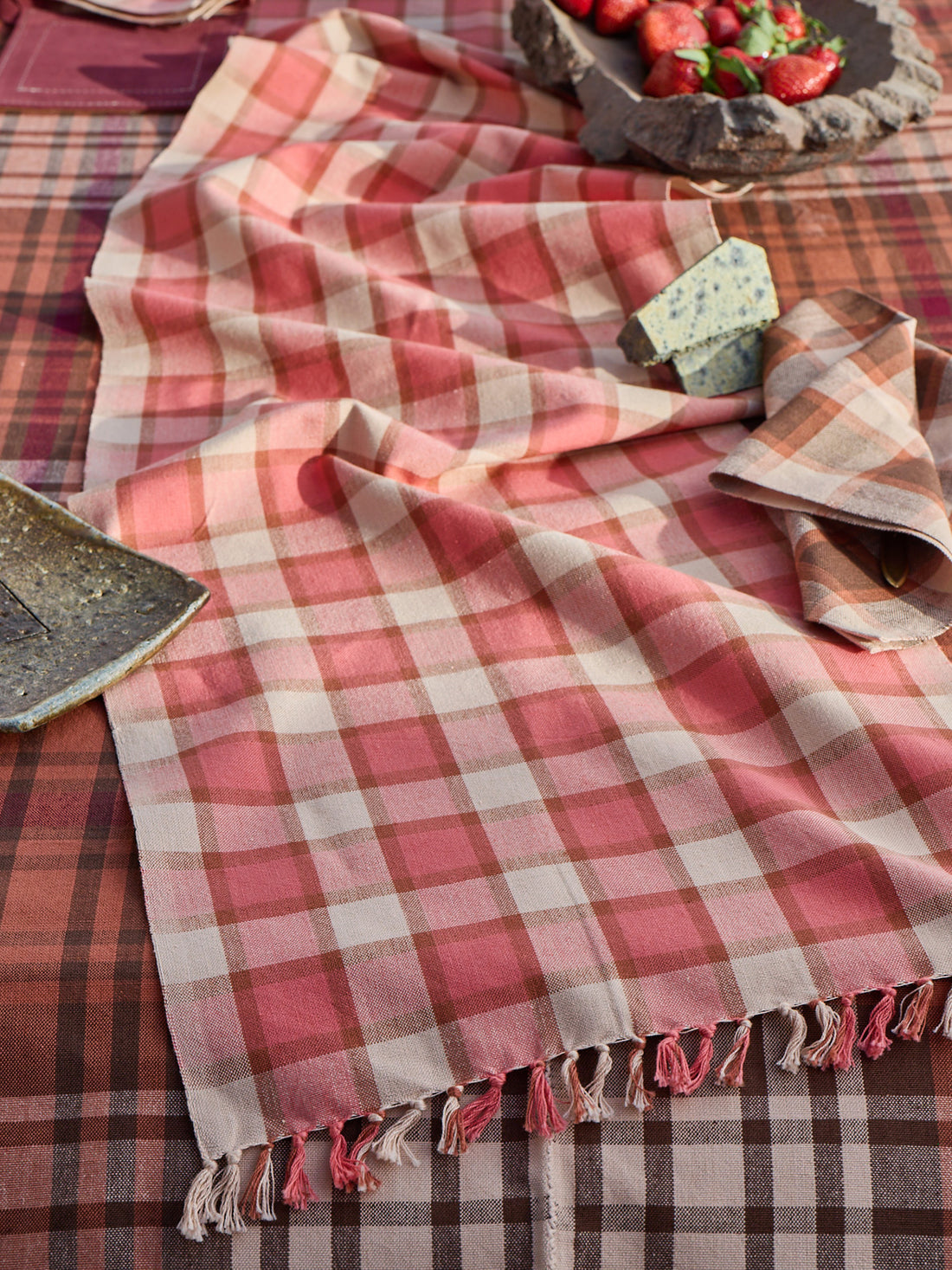 Plaid tablecloth with fringe on a table setting with strawberries and cheese.
