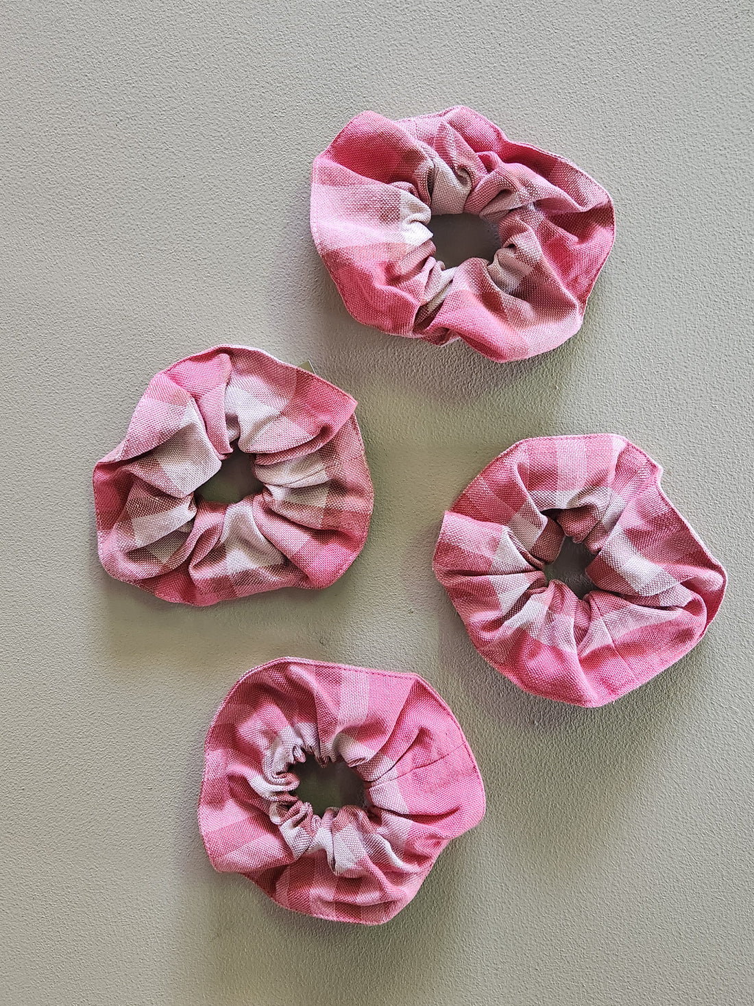 Four pink and white tie-dye scrunchies on a light gray background