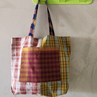 Plaid tote bag hanging on a green hook against a light gray wall.