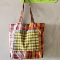 Colorful plaid tote bag hanging on a green hook against a plain wall.