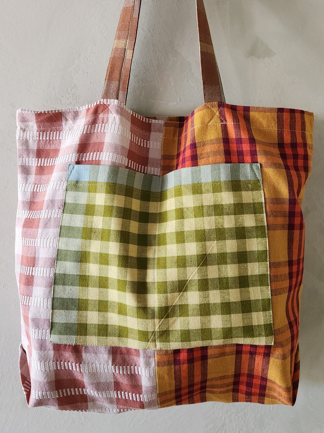 Multicolored plaid tote bag with a green checkered pocket on a light background