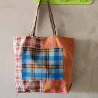 Colorful plaid tote bag hanging on a green hook against a beige wall.