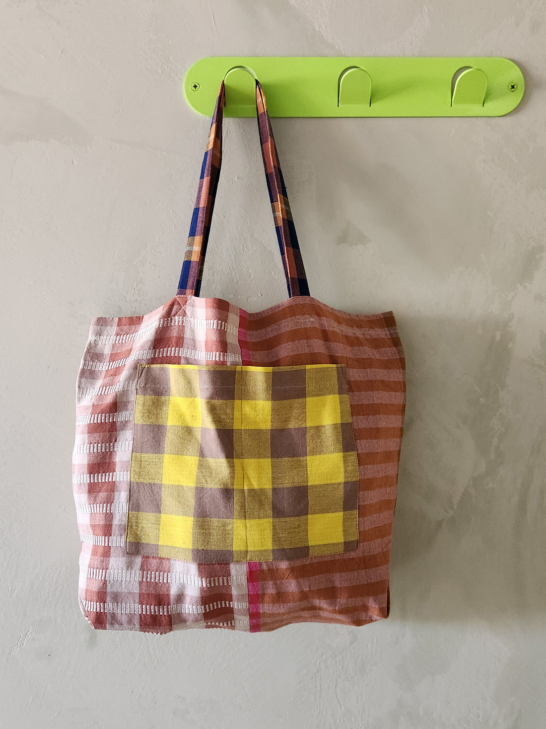Plaid bag hanging on a green hook against a gray wall