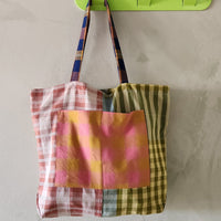 Colorful plaid tote bag hanging on a green wall hook against a plain background