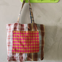 Plaid tote bag hanging on a green wall hook against a beige wall.