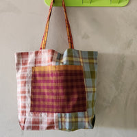 Plaid tote bag hanging on a green hook against a beige wall.