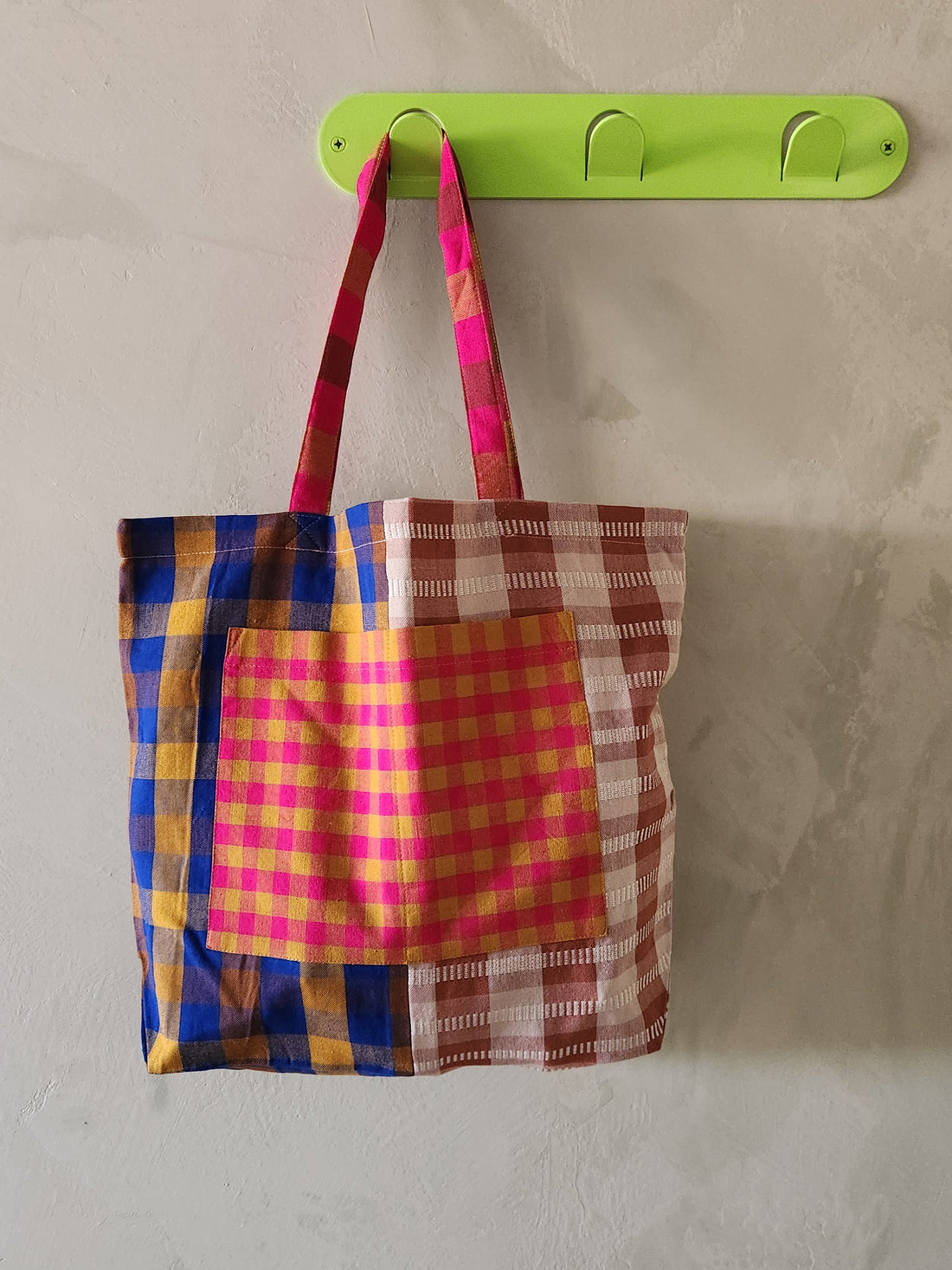 Colorful plaid bag hanging on a green hook against a plain wall.