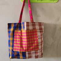 Colorful plaid bag hanging on a green hook against a plain wall.