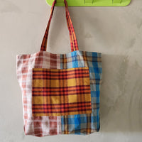 Plaid tote bag hanging on a green hook against a light gray wall.