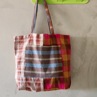 Colorful plaid tote bag hanging on a green wall hook against a plain background