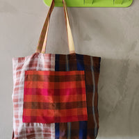 Colorful plaid tote bag hanging on a green wall hook against a neutral background