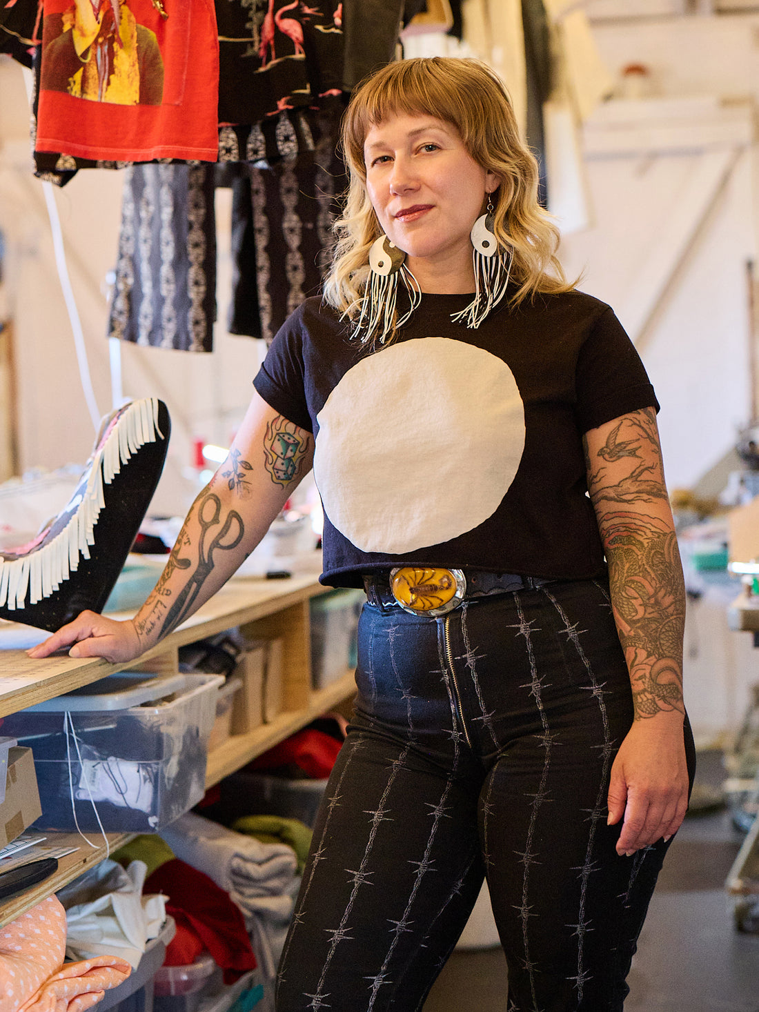 Person wearing a black t-shirt with a large white circle design, standing in a store with clothing racks in the background.