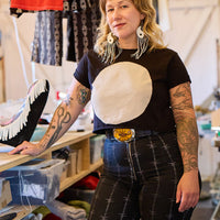 Person wearing a black t-shirt with a large white circle design, standing in a store with clothing racks in the background.