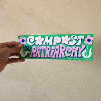Hand holding a bumper sticker with text and floral designs on a beige background