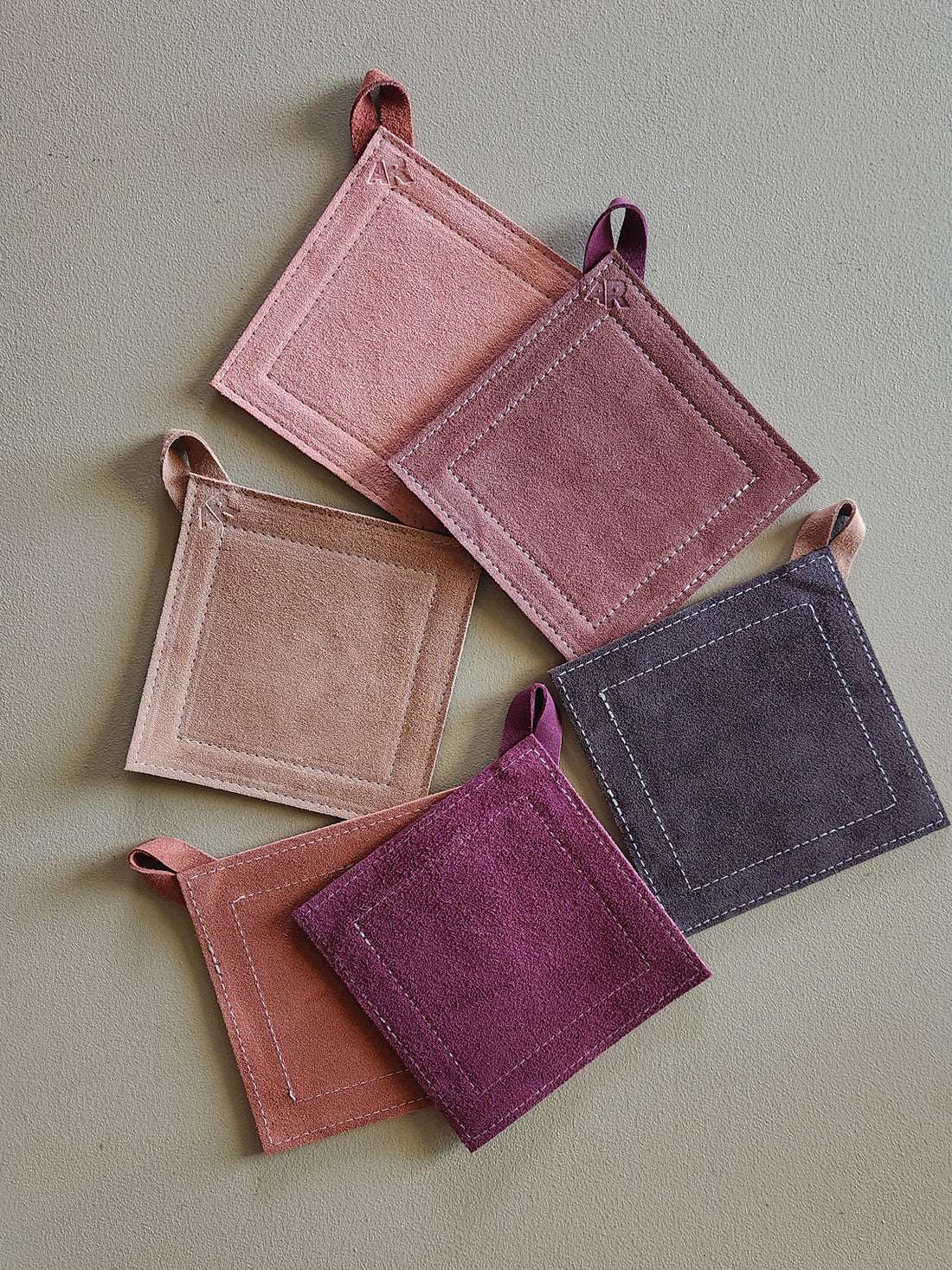 Set of five square potholders in various shades of purple on a light green background