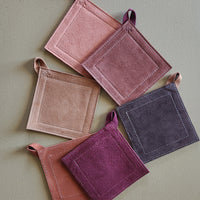 Set of five square potholders in various shades of purple on a light green background