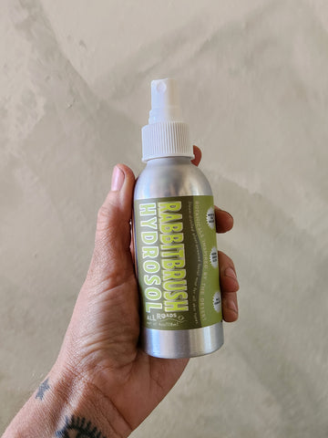 Hand holding a bottle of 'Rabbitbrush Hydrodual' with a beige background